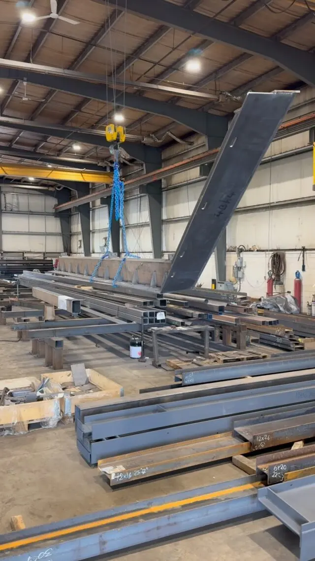 Overhead crane moving structural steel beams in the shop